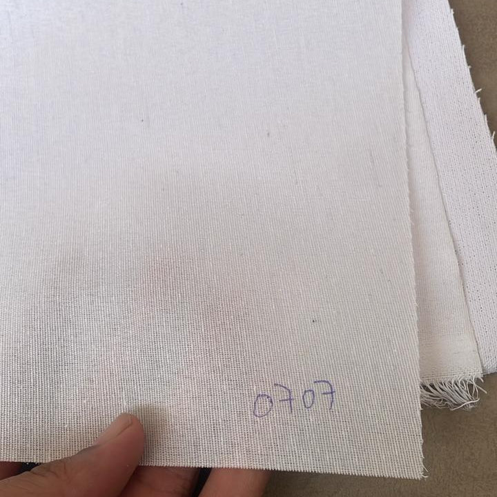 White interlining fabric swatch held by a hand on a brown surface